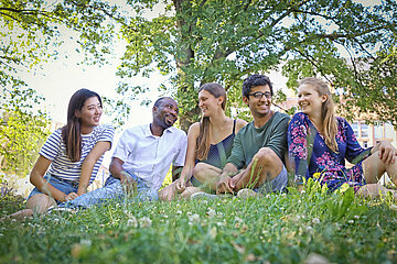 A group of students different nationalities sitting on the grass