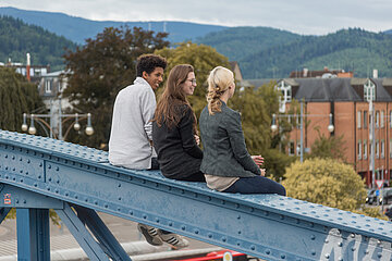 [Translate to Englisch:] Drei Studierenden unterschiedlicher Herkünfte sitzen auf der Blauen Brücke in Freiburg