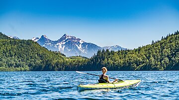 Woman with canoe in lake in the middle of forest and mountain