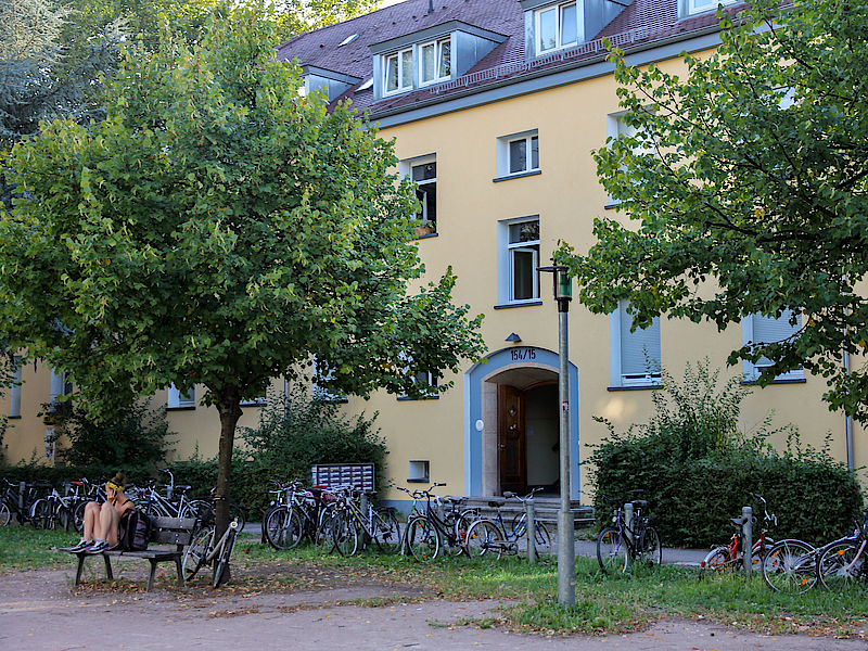 Wohnheim von außen mit Bäumen und Sitzbank