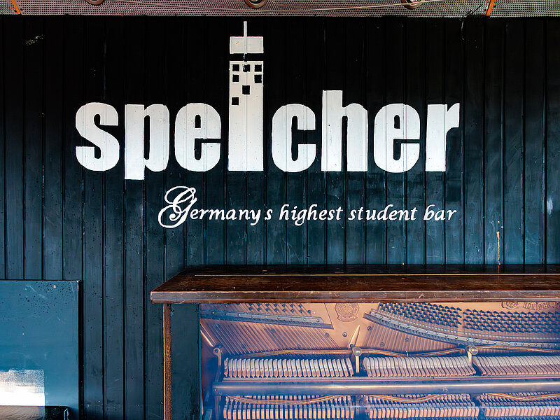 Schriftzug „Speicher – Germany’s highest student bar“ an Wand der Studentenbar über einem Klavier.